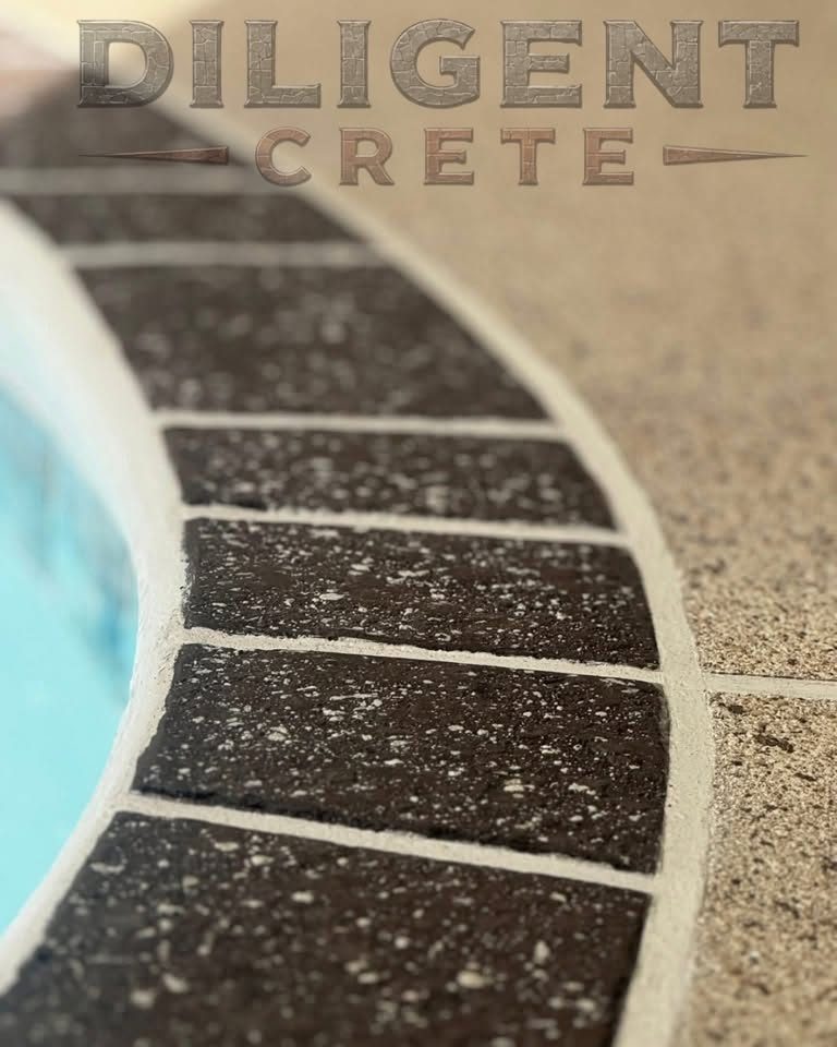 Close-up of dark brick-pattern concrete coping curving around a pool edge against a sand-speckled deck