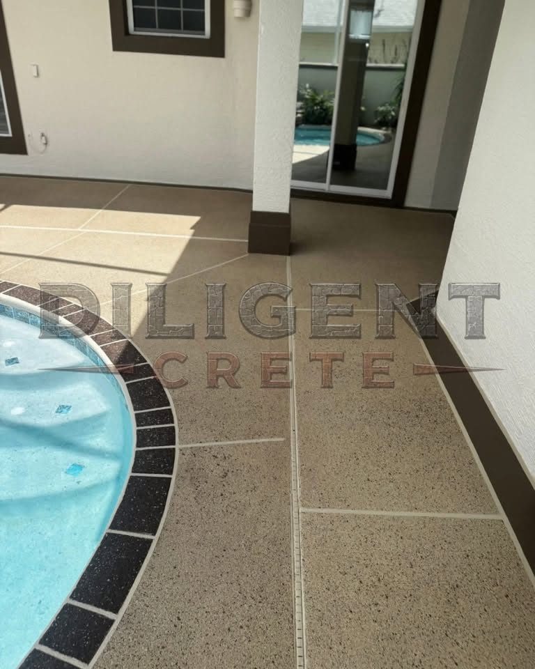 Sand-coloured textured concrete pool deck around a spa, with a dark brick-pattern coping band and scored tile lines